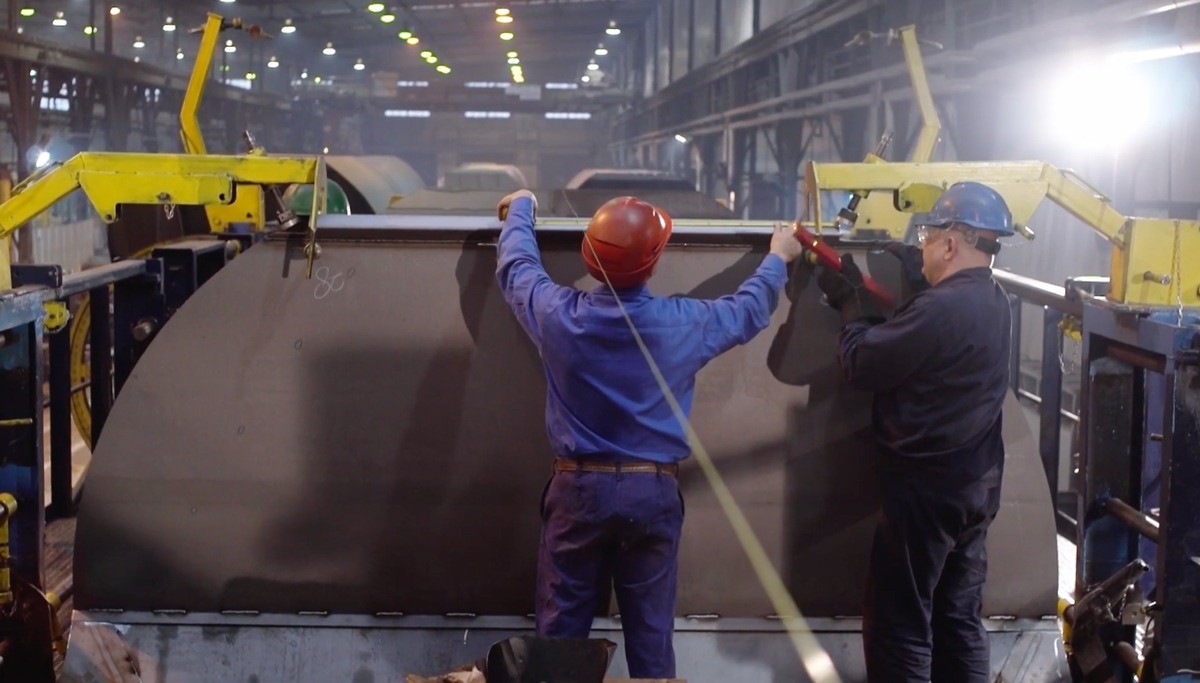 Two workers measuring a piece of metal.