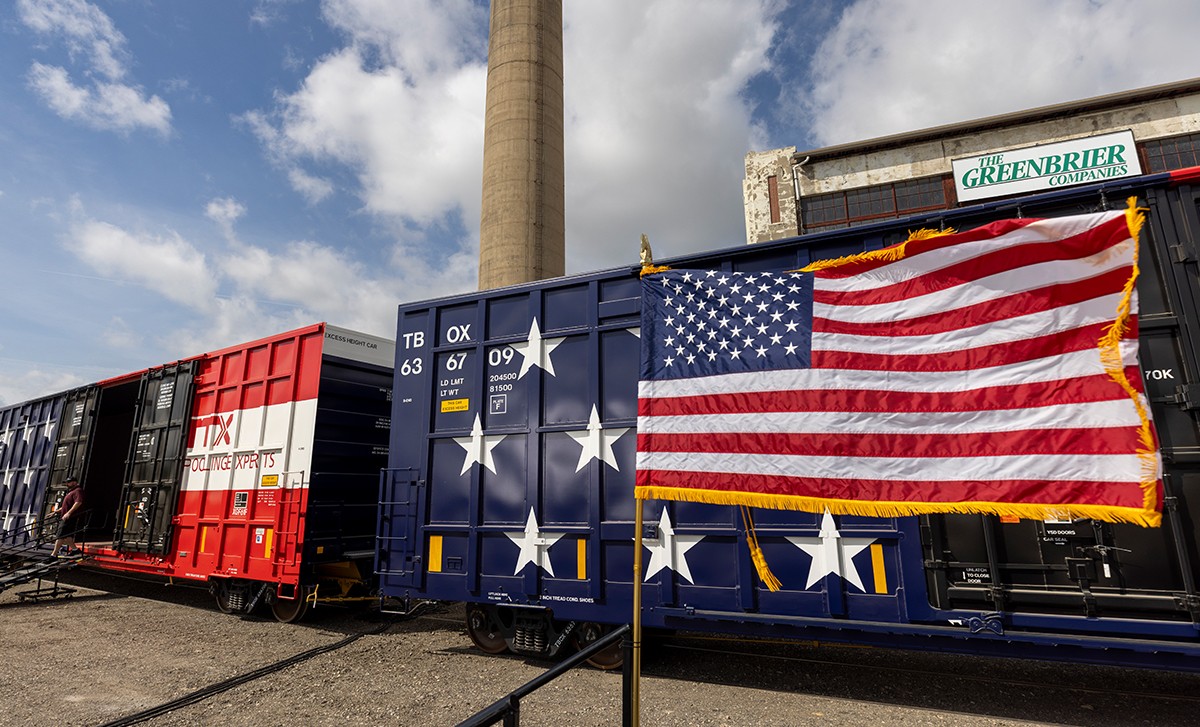 American flag flying in front of 2 boxcars painted with stars and stripes.